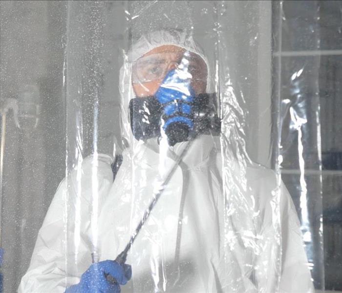 Person in PPE standing behind a plastic containment sheet. 